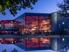 Die OsnabrückHalle, ein Veranstaltungszentrum, erleuchtet in den Abendstunden und sich im Wasser widerspiegelnd.